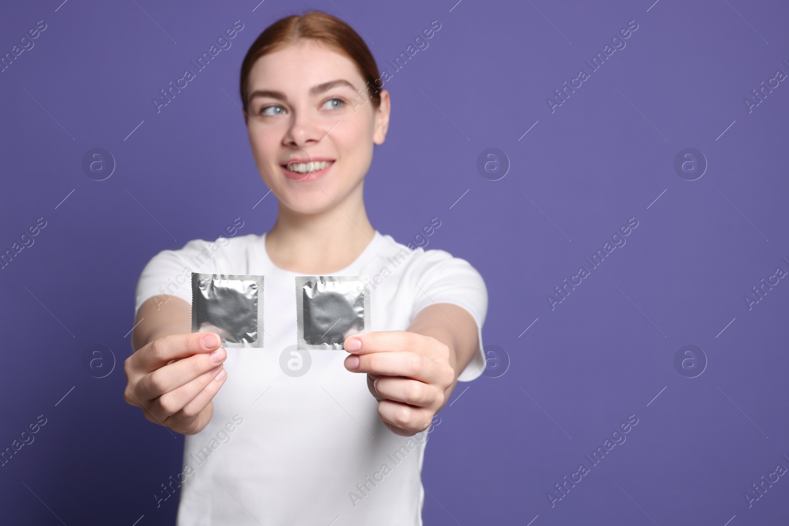 Photo of Woman holding condoms on purple background, space for text. Safe sex