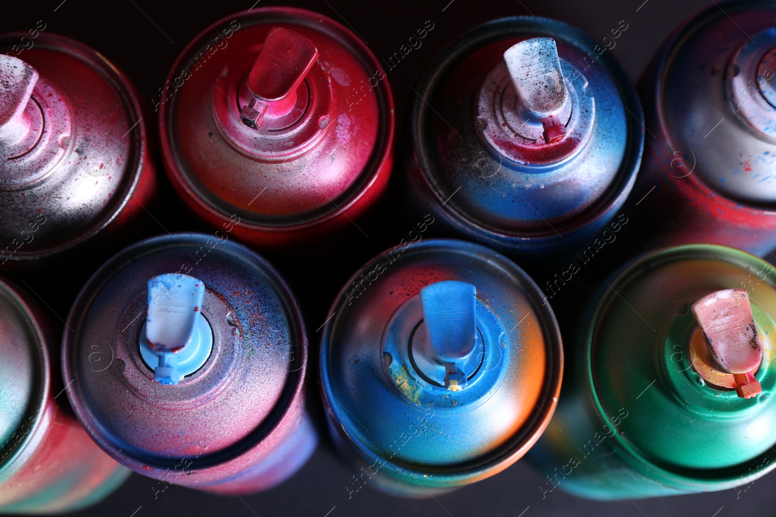 Photo of Many spray paint cans on black background, above view