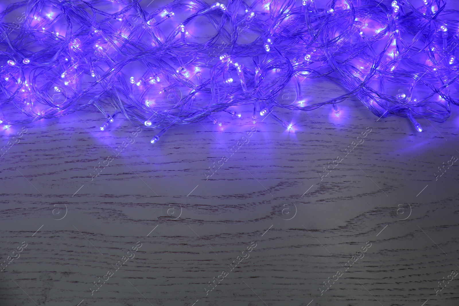 Photo of Blue Christmas lights on white wooden background, top view. Space for text