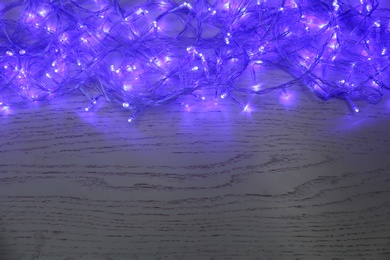 Blue Christmas lights on white wooden background, top view. Space for text