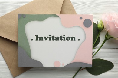Photo of Card with word Invitation, envelope and flowers on white wooden background, flat lay