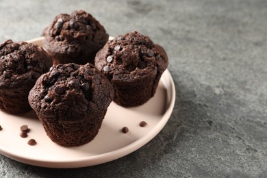 Photo of Delicious chocolate muffins on grey textured table, space for text