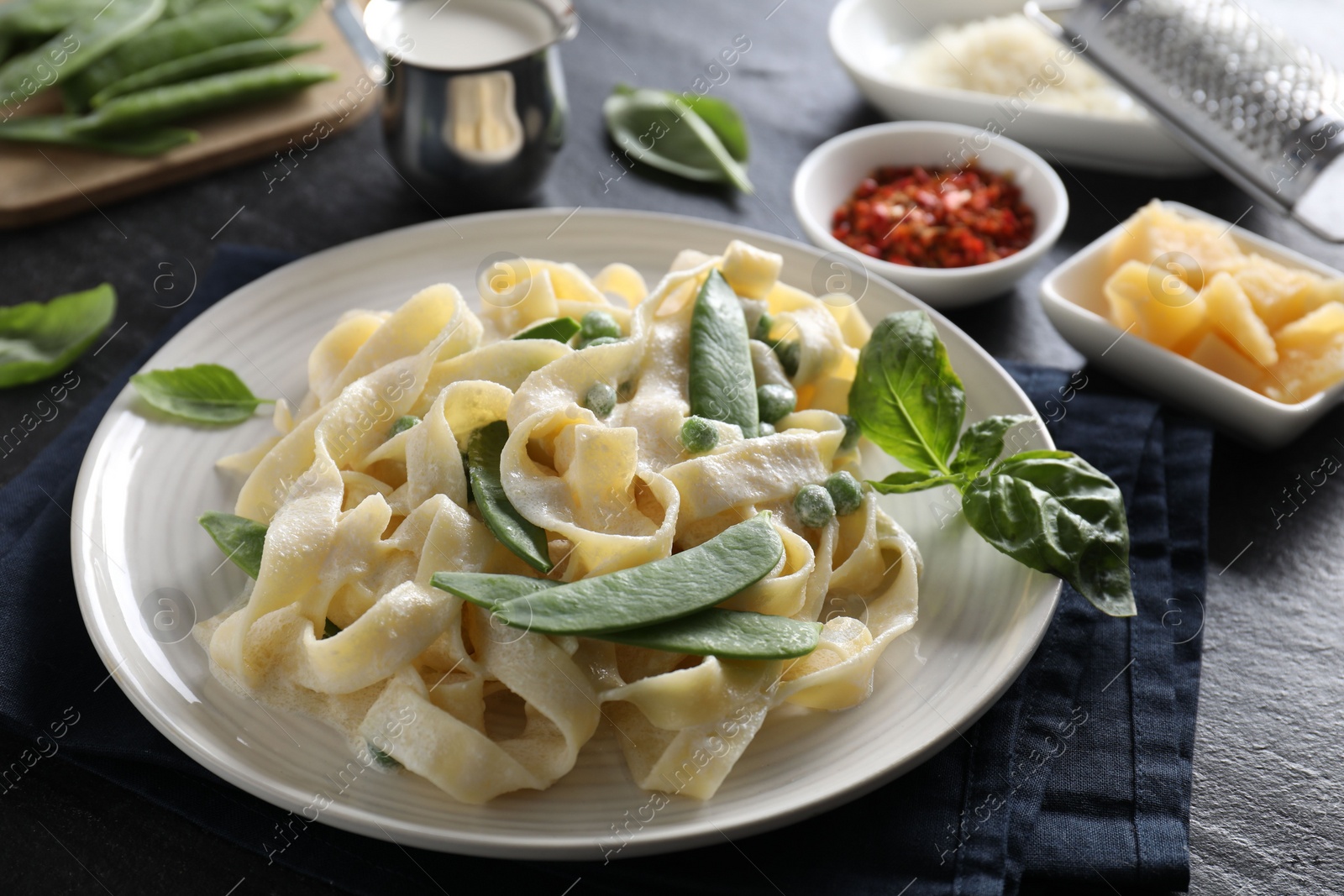 Photo of Delicious pasta with green peas and creamy sauce on black table