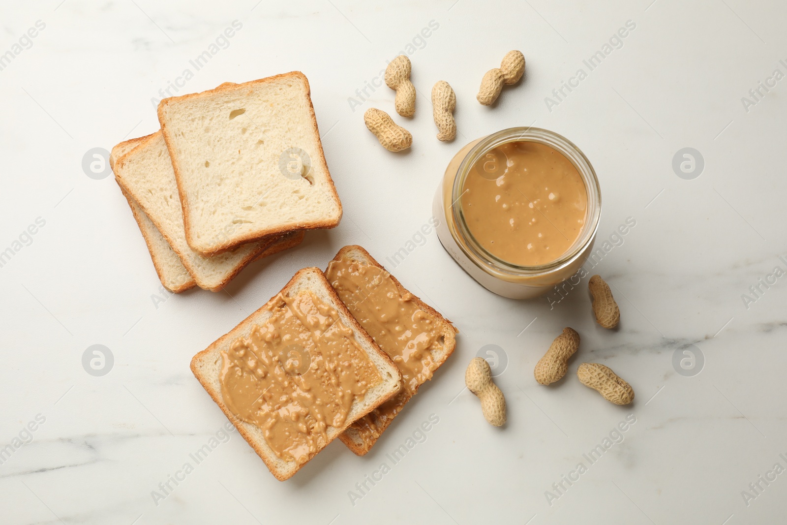 Photo of Delicious toasts with peanut butter and nuts on white marble table, flat lay