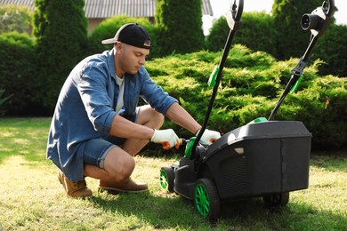 Young man with screwdriver fixing lawn mower in garden on sunny day
