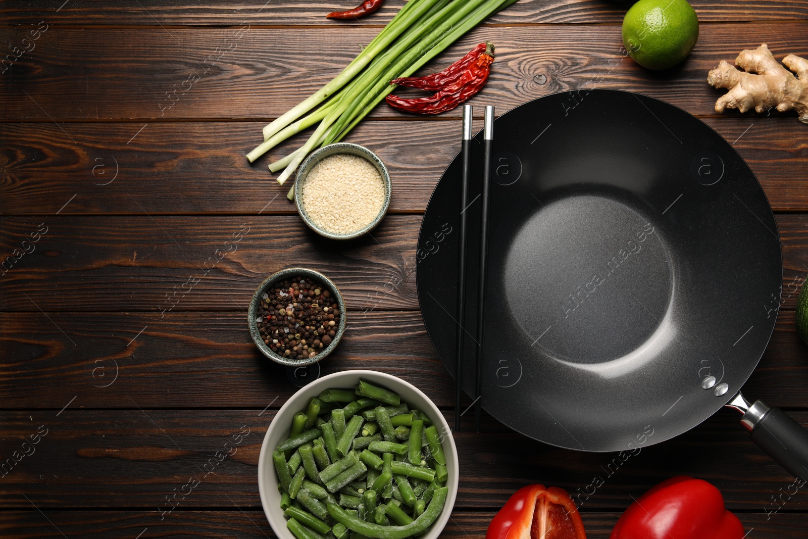 Photo of Black wok, chopsticks and products on wooden table, flat lay. Space for text