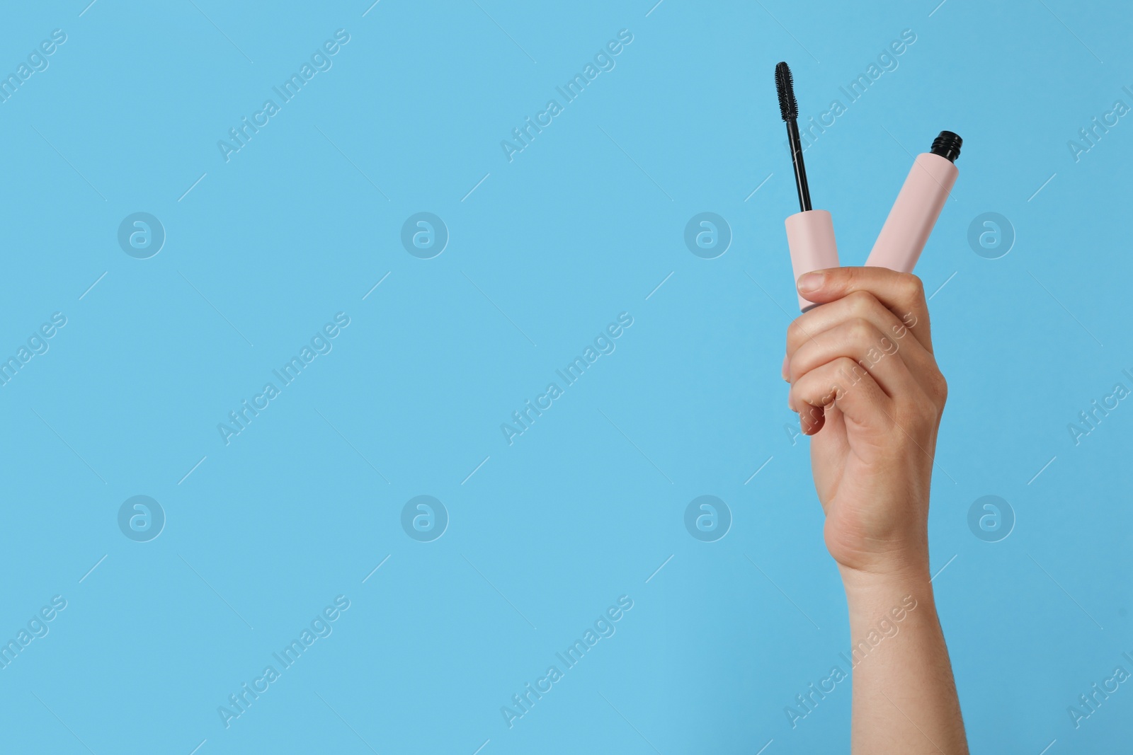 Photo of Woman holding mascara on light blue background, closeup. Space for text