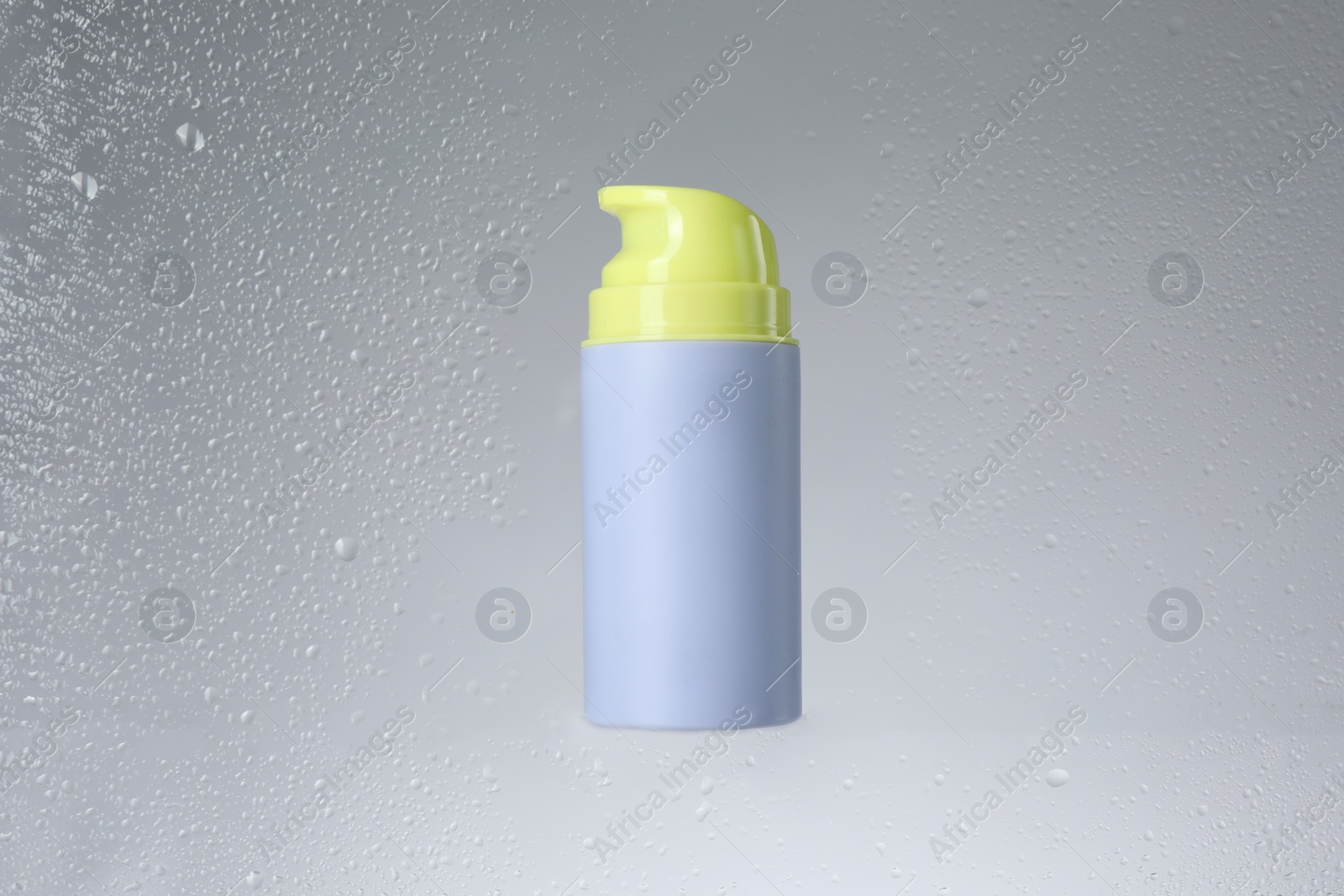 Photo of Bottle with moisturizing cream on light background, view through wet glass