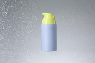 Bottle with moisturizing cream on light background, view through wet glass