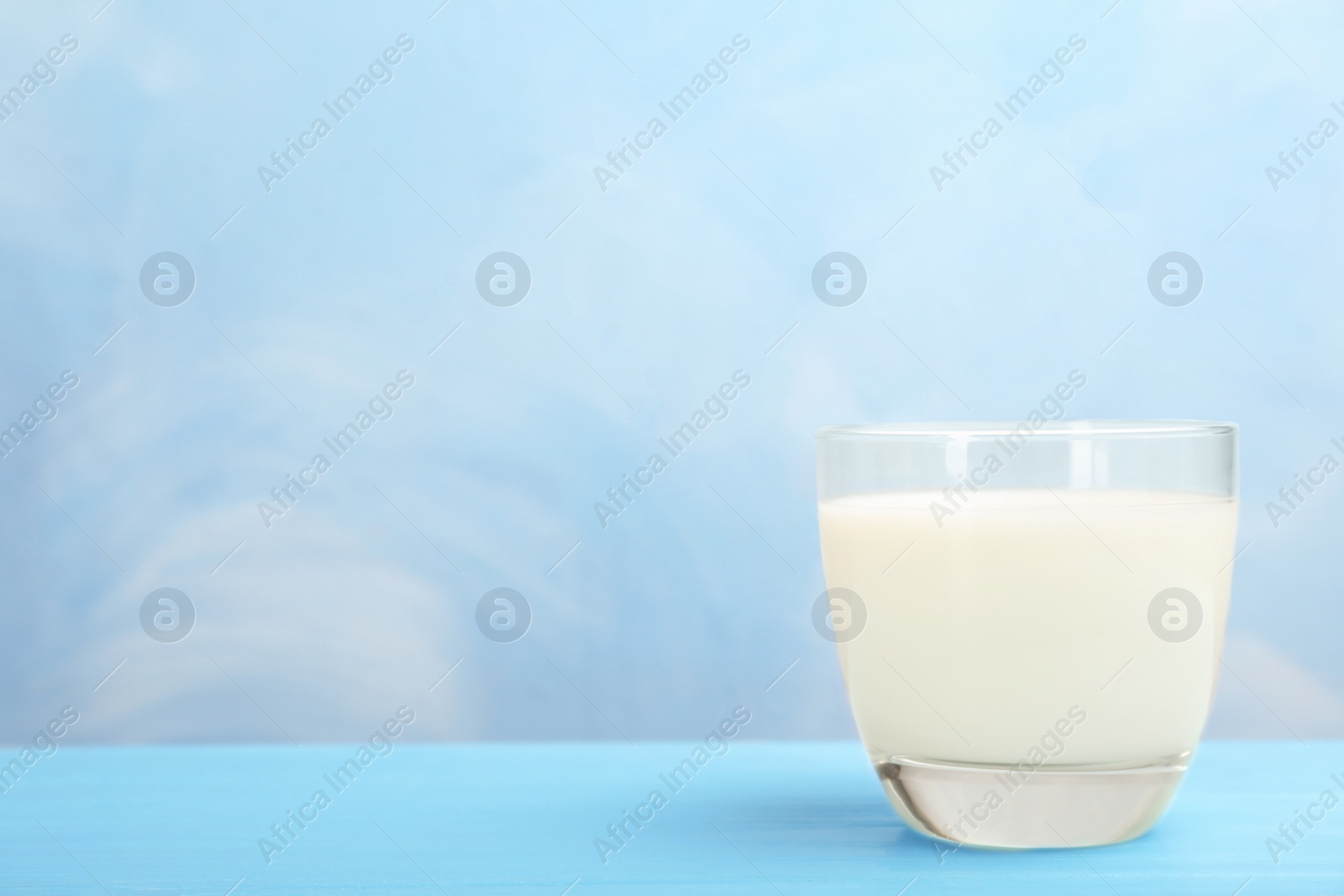 Photo of Glass with fresh milk on table against color background. Space for text