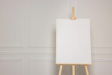 Photo of Wooden easel with blank canvas near white wall. Space for text