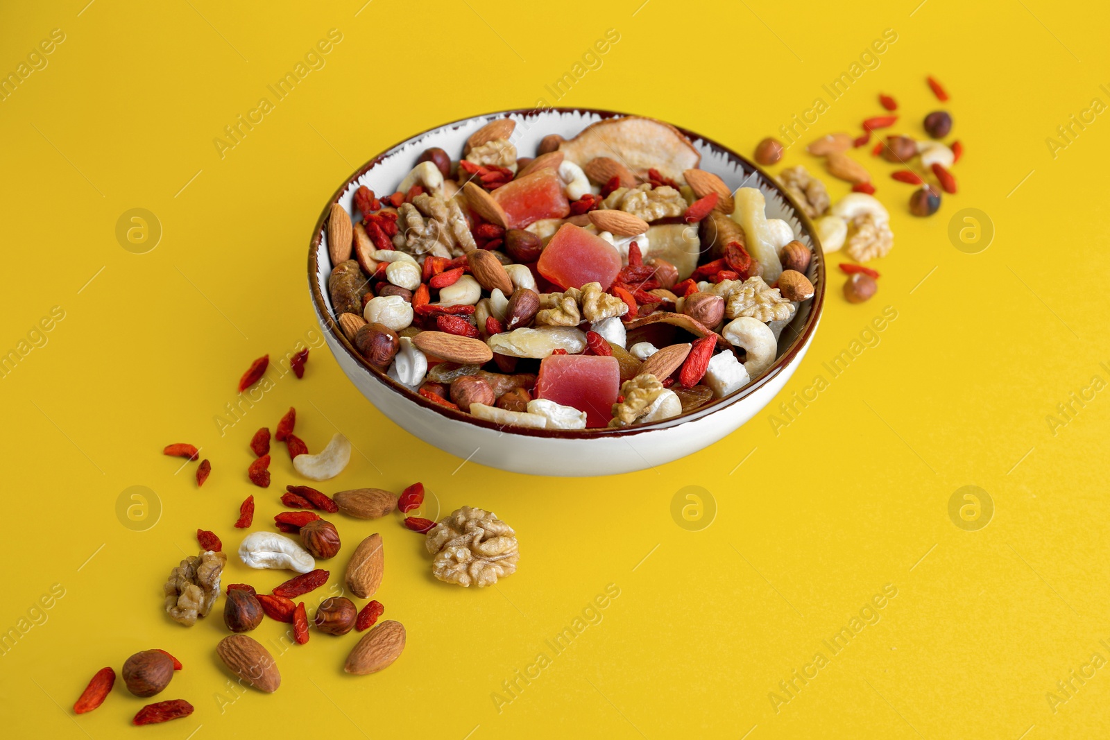 Photo of Bowl with mixed dried fruits and nuts on yellow background