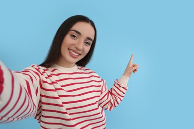 Photo of Smiling young woman taking selfie on light blue background, space for text