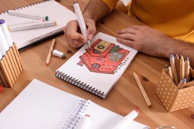 Photo of Man drawing in sketchbook with felt tip pen at wooden table, closeup