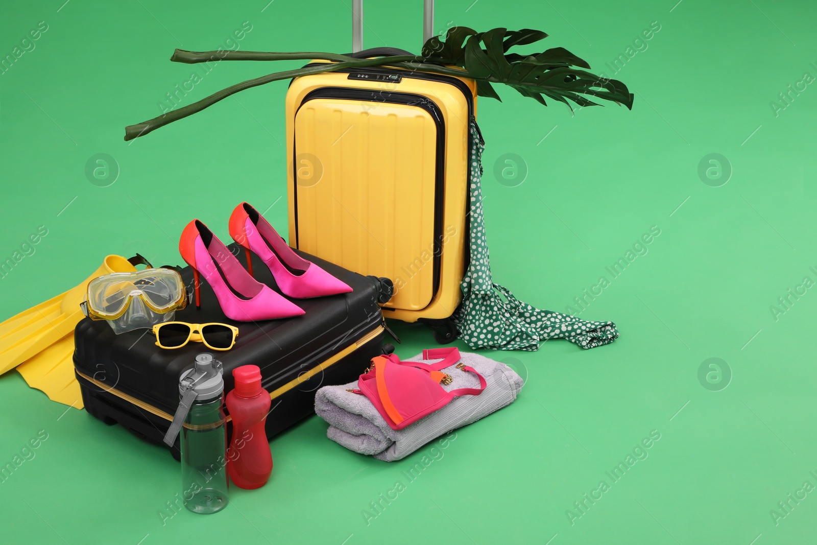 Photo of Suitcases, beach accessories and tropical leaves on green background, space for text. Summer vacation