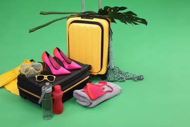 Photo of Suitcases, beach accessories and tropical leaves on green background, space for text. Summer vacation
