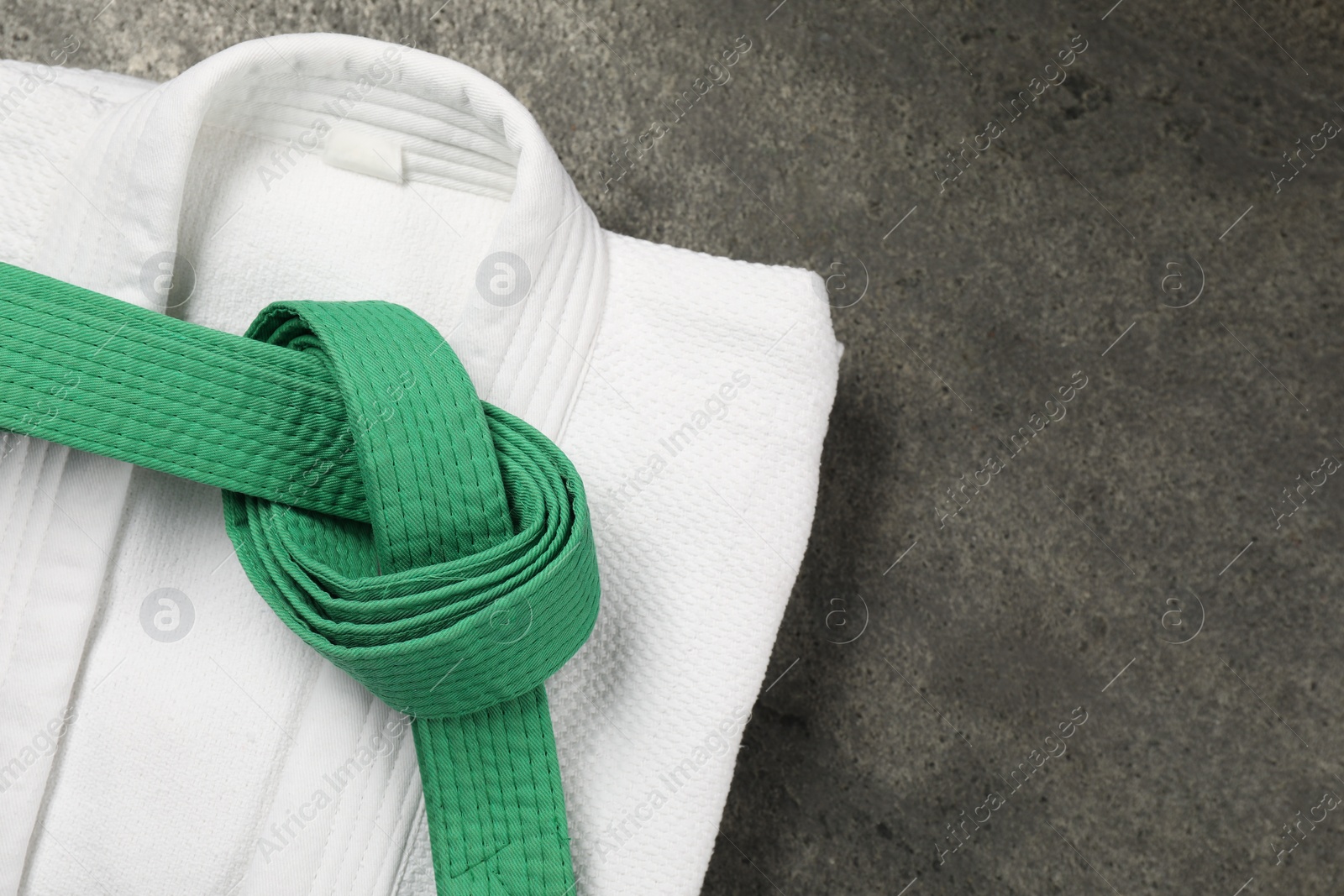 Photo of Green karate belt and white kimono on gray textured background, top view. Space for text