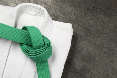 Green karate belt and white kimono on gray textured background, top view. Space for text