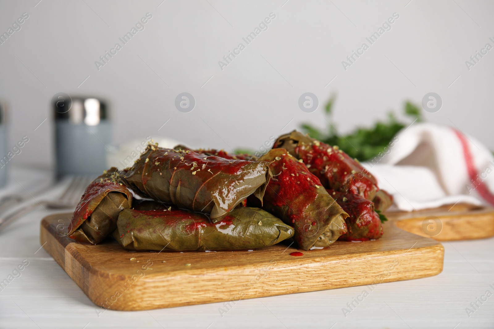 Photo of Delicious stuffed grape leaves with tomato sauce on white wooden table