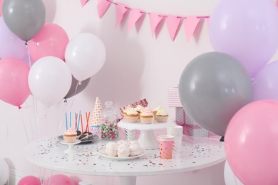 Photo of Party treats and items on table in room decorated with balloons