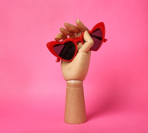 Photo of Wooden mannequin hand with stylish heart shaped glasses on color background
