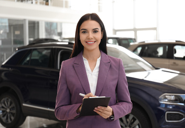 Young saleswoman with clipboard in modern car salon