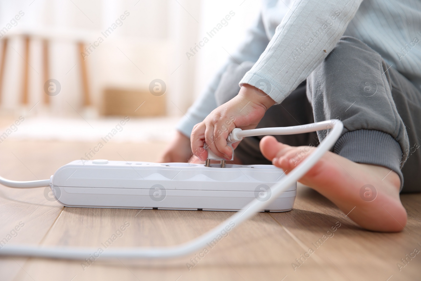 Photo of Little child playing with power strip and plug on floor indoors, closeup. Dangerous situation