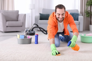 Photo of Young man cleaning carpet at home