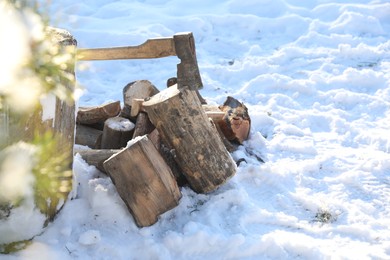 Photo of Metal axe in wooden log and pile of wood outdoors on sunny winter day. Space for text