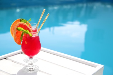 Refreshing cocktail in glasses near outdoor swimming pool on sunny day. Space for text