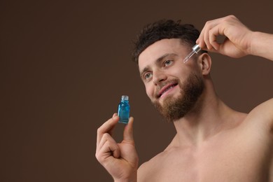 Photo of Handsome man applying serum onto his face on brown background, space for text