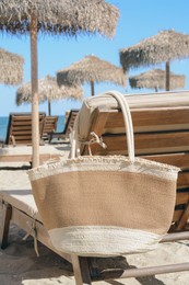 Photo of Straw bag on wooden sunbed near sea. Beach accessory