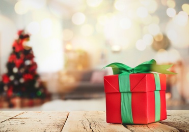 Image of Christmas gift box on wooden table in room, bokeh effect. Space for text