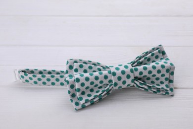 Stylish bow tie with green polka dot pattern on white wooden table, closeup. Space for text