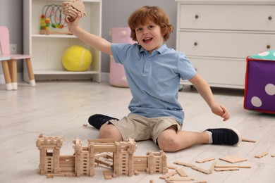 Photo of Emotional boy playing with wooden construction set on floor in room. Child's toy