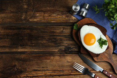 Photo of Tasty fried egg with parsley and rye bread on wooden table, flat lay. Space for text