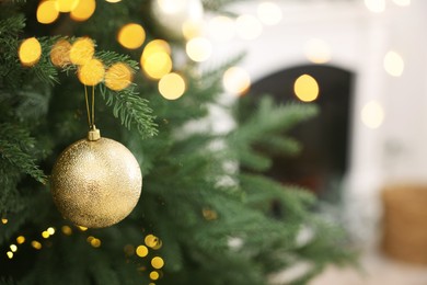 Photo of Christmas ball hanging on fir tree branch indoors, closeup. Space for text