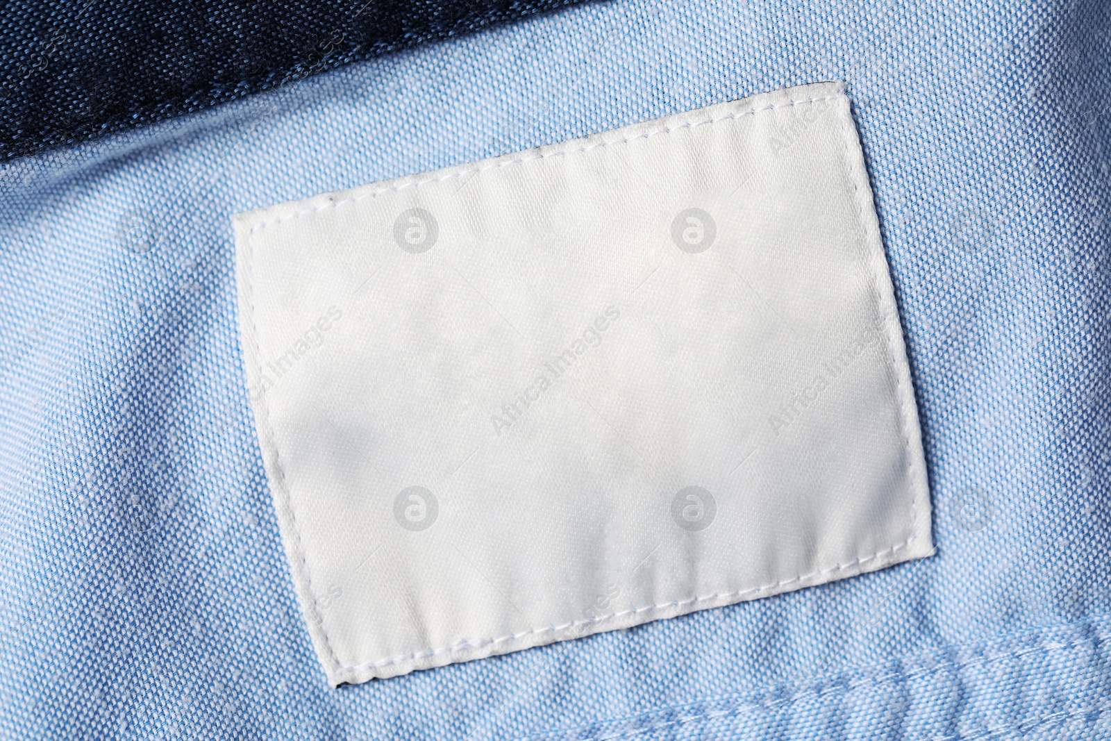 Photo of Empty clothing label on light blue garment, top view