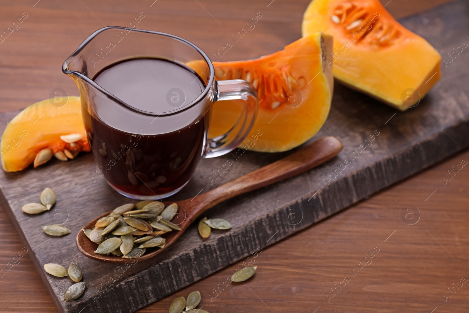 Photo of Fresh pumpkin seed oil in glass pitcher on wooden table. Space for text