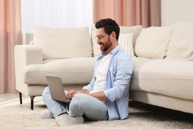 Photo of Man using laptop on floor near sofa at home