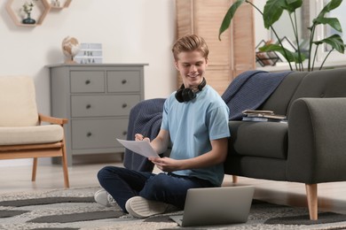Online learning. Smiling teenage boy writing essay near laptop at home