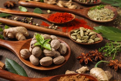 Photo of Different herbs and spices with spoons on wooden table, closeup