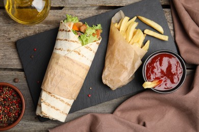 Photo of Delicious chicken shawarma and French fries served on wooden table, flat lay