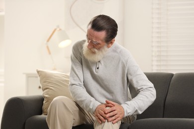 Senior man suffering from knee pain on sofa at home. Rheumatism symptom