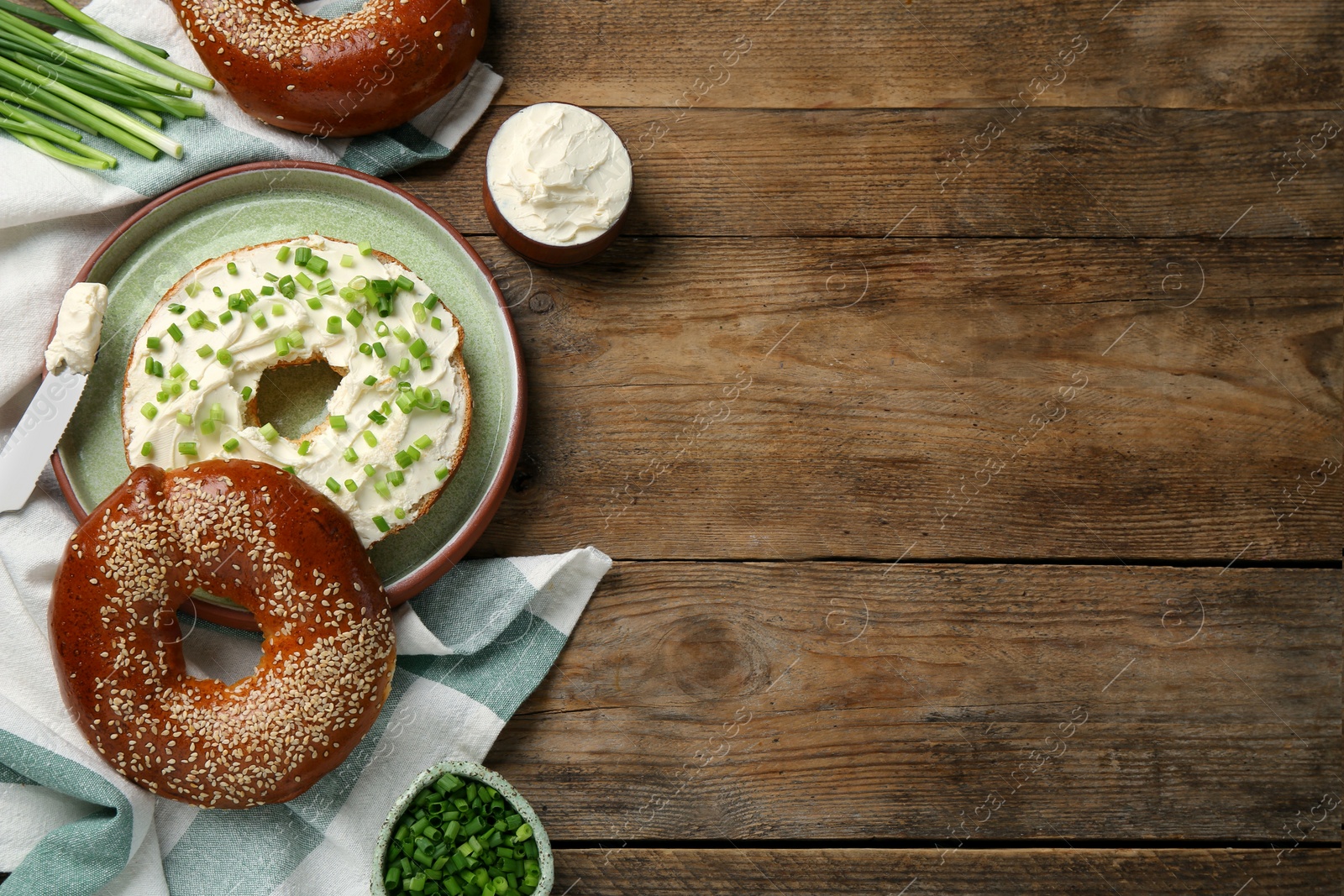 Photo of Delicious bagel with cream cheese and green onion on wooden table, flat lay. Space for text