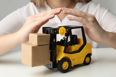 Woman covering toy forklift at white table, closeup. Logistics and wholesale concept