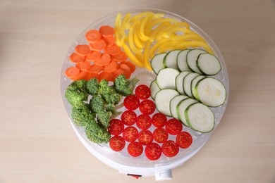 Cut vegetables in fruit dehydrator machine on wooden table, top view