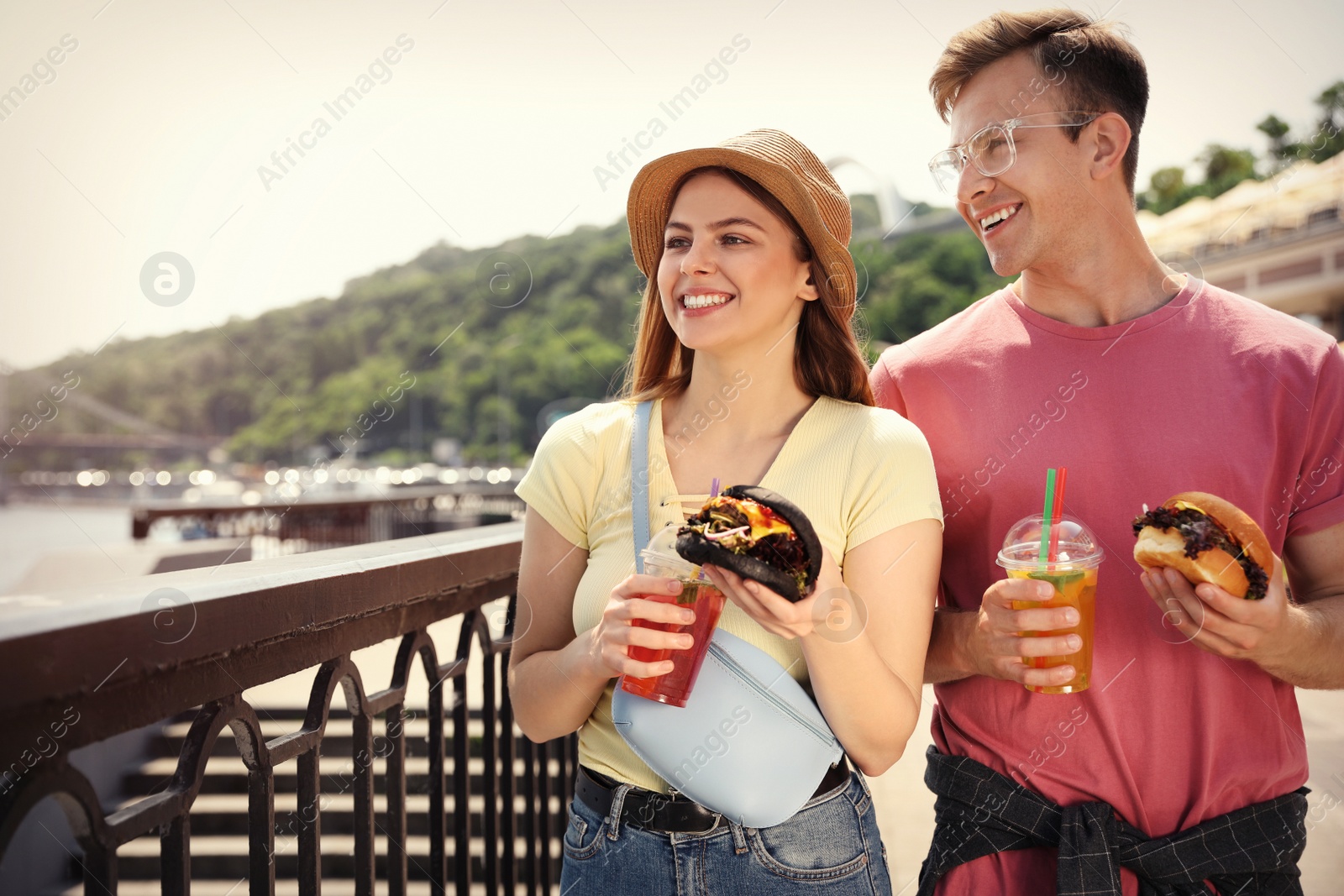 Photo of Young happy couple with burgers walking on city street. Space for text