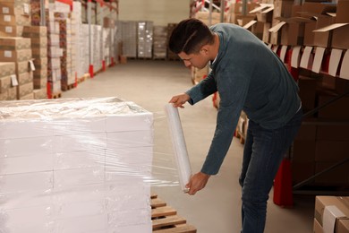 Worker wrapping boxes in stretch film at warehouse