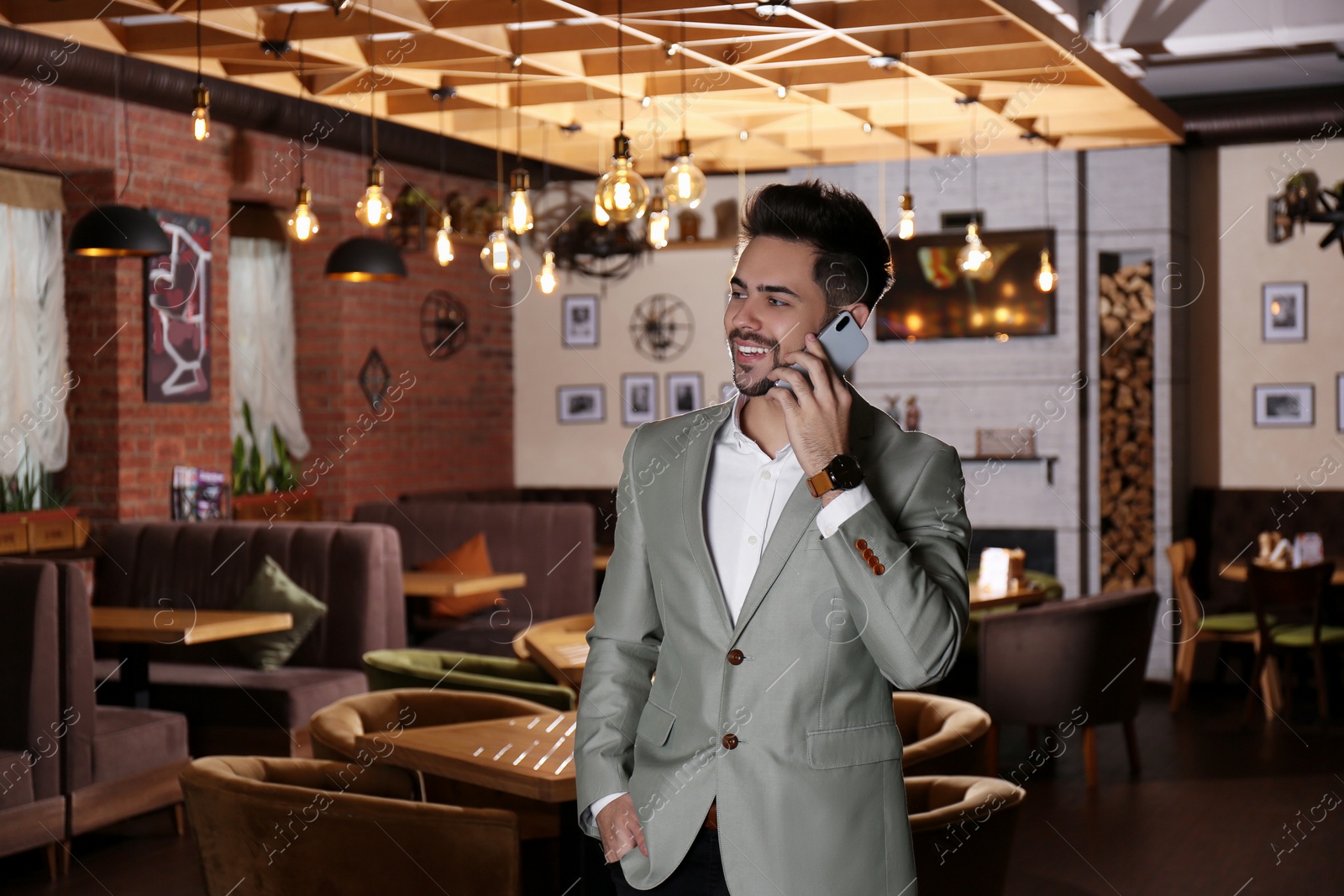 Photo of Young business owner talking on phone in his cafe